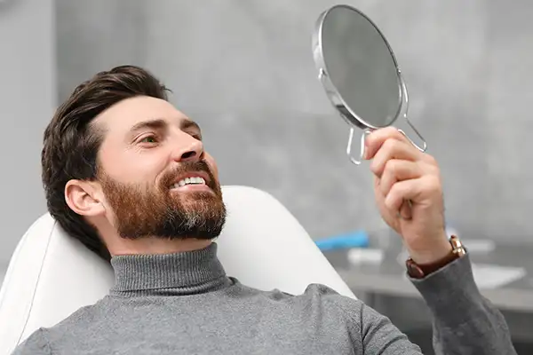 Smiling dental patient leaning back in exam chair and looking up into mirror Smiling dental patient leaning back in exam chair and looking up into mirror